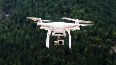 White Quadcopter Drone Hovering in Front of a Forested Background With Camera Attached