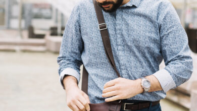 A Man is Looking at a Mini Bag for Men—a Compact Crossbody Leather Mini Bag With a Flap—held in Front of Him, Showing Its Detail